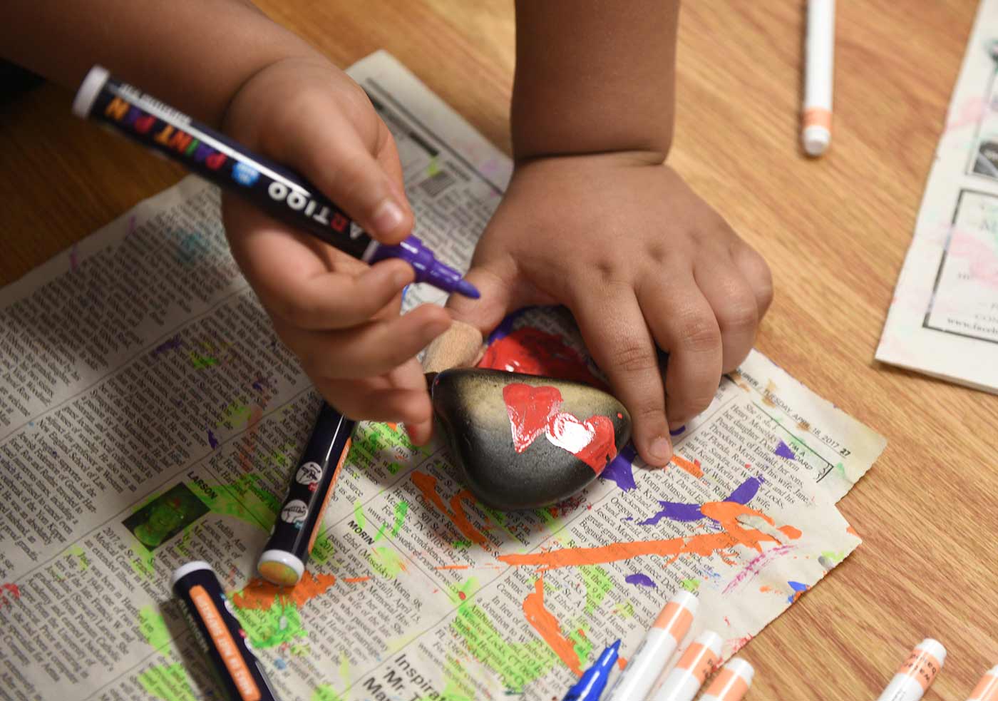 Young student decorates a rock with paint markers on the floor of a classroom