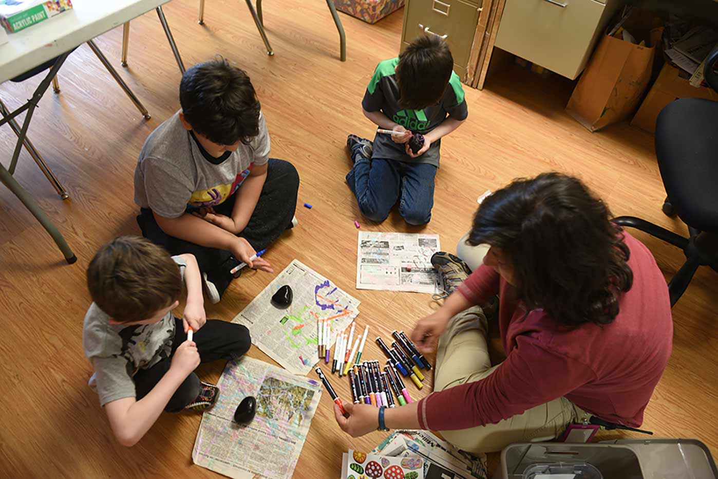 Three young Natchaug students work with a teacher to decorate rocks with paint markers