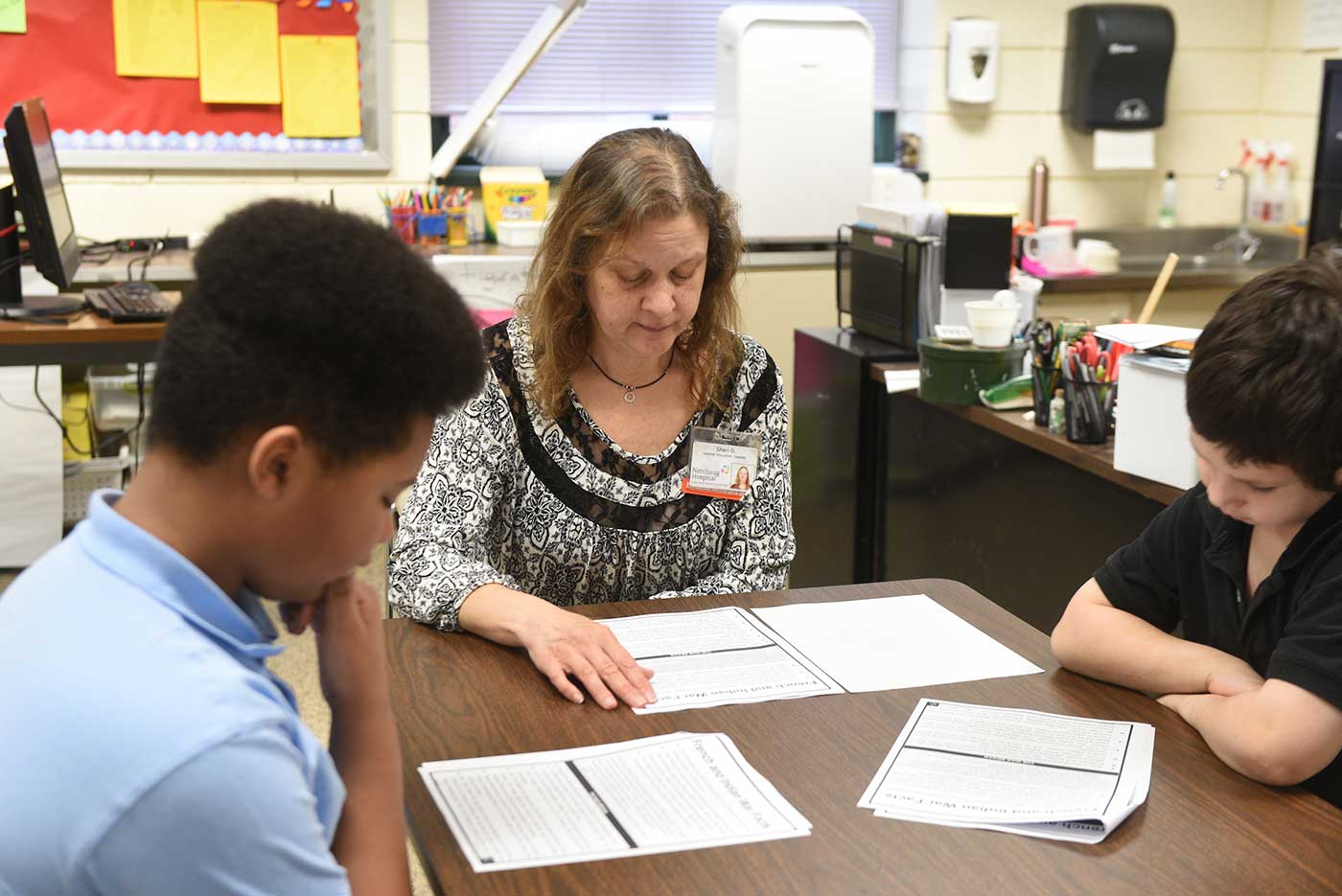 Natchaug teacher works with two students while they read packets during class