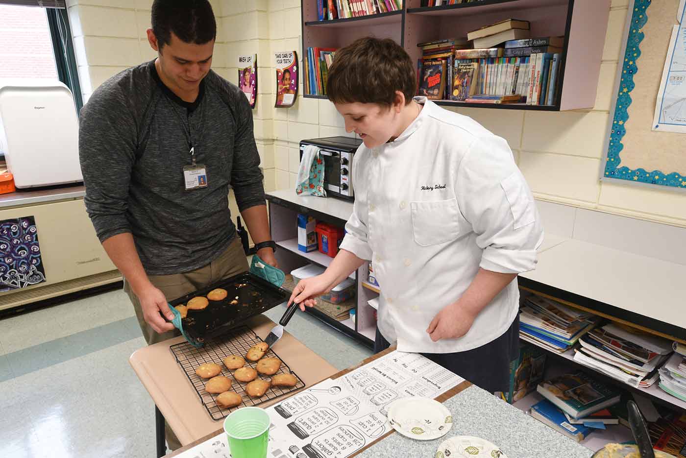 Two Natchaug students take cookies from a cookie sheet and place them on a cooling rack during cooking class